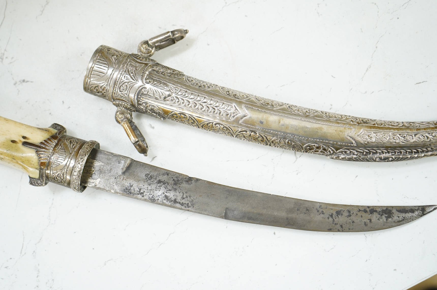 A silver mounted Moroccan dagger jambya, with silver sheath and hilt, mounts chased with foliate and floral designs, and one piece bone grip, blade as found, overall length 42cm